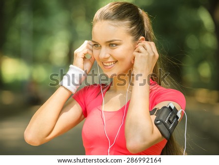 Portrait of pretty young woman listening to music after running. Training outdoors in the morning.