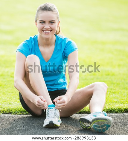 Attractive sporty girl sitting on the road and tie shoelaces.