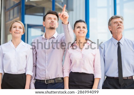 Group of successful office workers standing in front of office and looking at something.