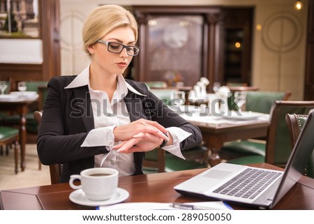Confident businesswoman sitting at the table in cafe and looking on watches.