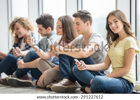 College friends sitting on the floorin line and watching pics on their gadgets at break. Side view.