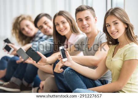 College friends sitting on the floor and watching pics on their gadgets at break.