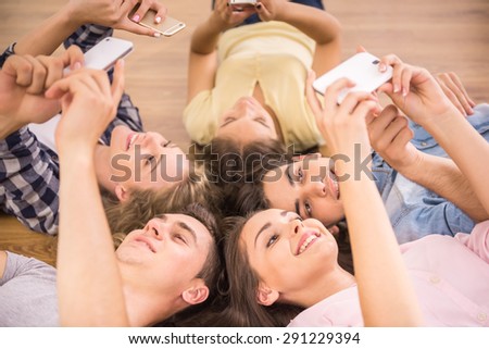 Education, people and technology concept - close up of students or friends with smartphones lying on floor in circle.