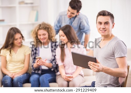 Group of young positive friends sitting at sofa and using their phones. Education concept. Front view.