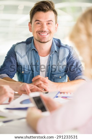 Young handsome man dressed casual sitting at the table in office and smiling to camera.
