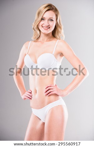 Perfect body. Smiling beautiful blonde in white bikini posing at studio, gray background.