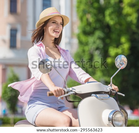 Young pretty girl driving scooter in european city. Side view.