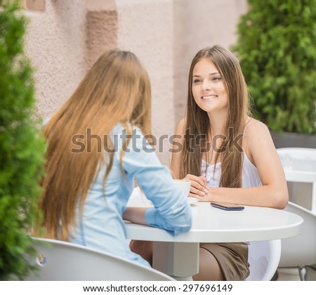 Happy young women sitting at urban cafe in summer and sharing latest news.