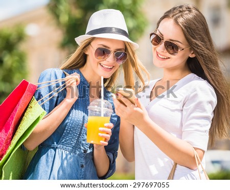 Young girls with shopping bags looking at phone and smiling. Blond hair woman holding a glass of juice.