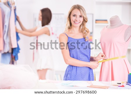 Fashion designers at work. Beautiful young woman looking at camera and smiling while her colleague standing on background.