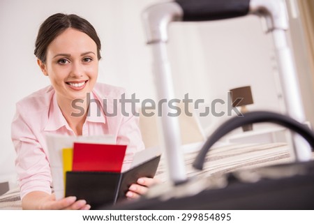 Beautiful business woman holding her documents while lying on bed near suitcase at the hotel room.