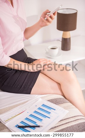 Business woman looking at phone while sitting on bed at the hotel room. Close-up.