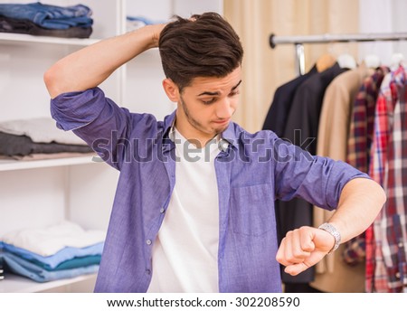 Young man checking the time and holding hand in hair while standing in dressing room.
