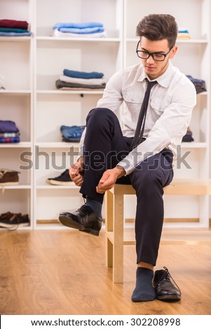 Stylish man in glasses tying shoe laces while sitting on chair at the dressing room.