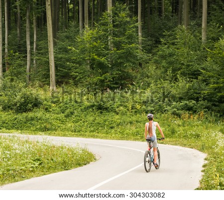 Young woman in helmet riding on mountain bicycle on the forest road. Back view.