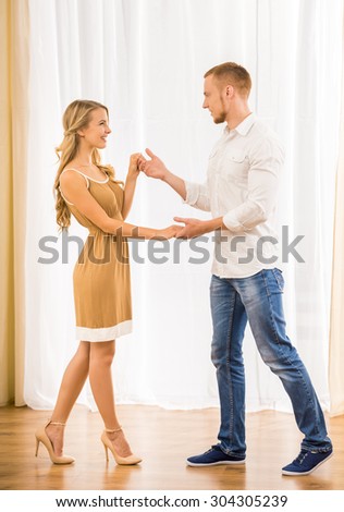 Beautiful couple dancing at home and looking to each other against window.