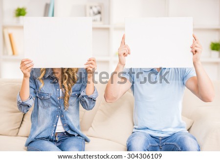 Couple sitting on sofa at home and closing their faces with papers.