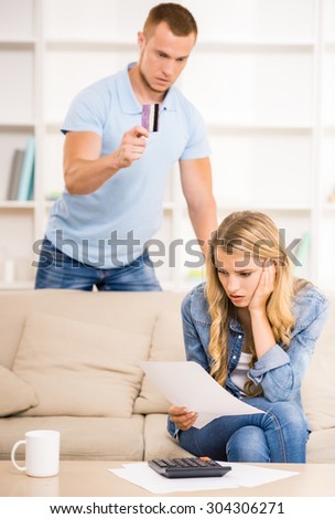 Woman calculating great expenses while her husband holding credit card and arguing with her.