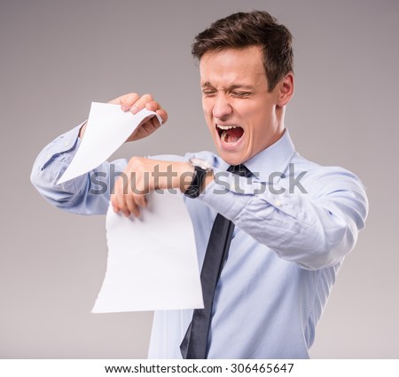 Emotional young businessman tearing paper on a gray background
