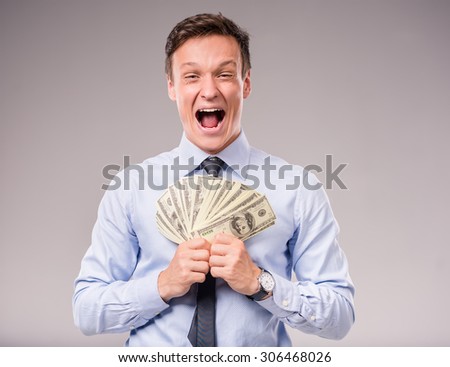 Young businessman holding more money on a gray background