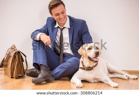 Smiling young businessman with his dog sitting on floor.