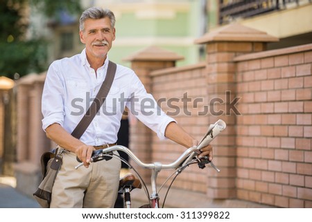 Senior man with his bike in the street, in town. Concept of active life elderly people.