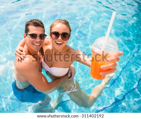 Top view of young couple relaxing in resort swimming pool and drinking cocktails.
