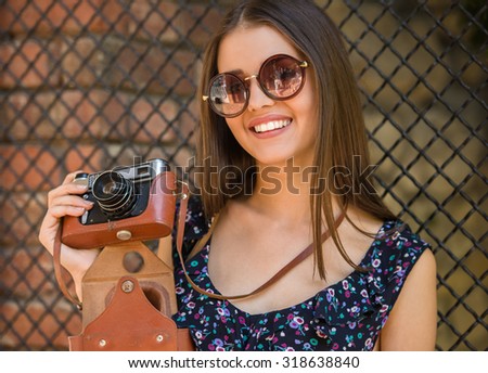 Happy young woman with old fashioned camera standing outdoors and smiling.
