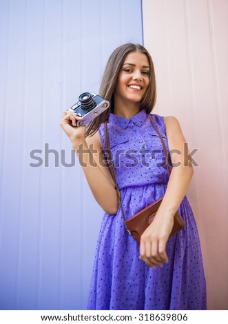 Young beautiful woman with old-fashioned camera standing against colorful wall.