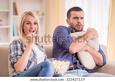 Loving young couple at home sitting on the couch, watch TV and eat popcorn
