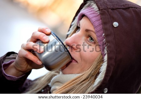 young female packed in a warm coat with hood drinking hot tea
