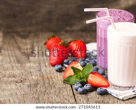 two glasses of milk shakes and fresh berries on a dark wooden background