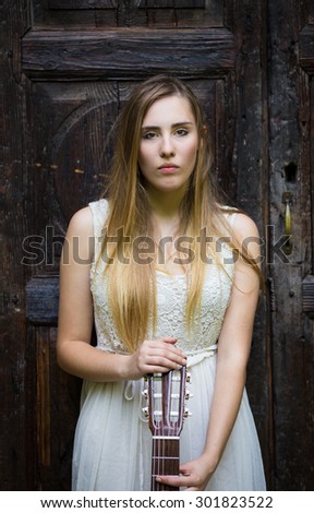 Pretty blonde girl in white dress playing guitar on rural outdoor