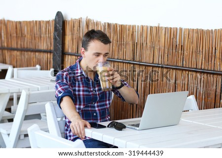 Successful freelancer drink his coffee while work on laptop computer in tropic cafe, stylish hipster use modern device