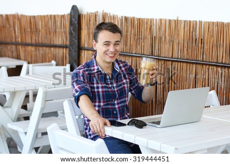 Successful freelancer drink his coffee while work on laptop computer in tropic cafe, young businessman smiling during breakfast in cafe,stylish hipster use modern device