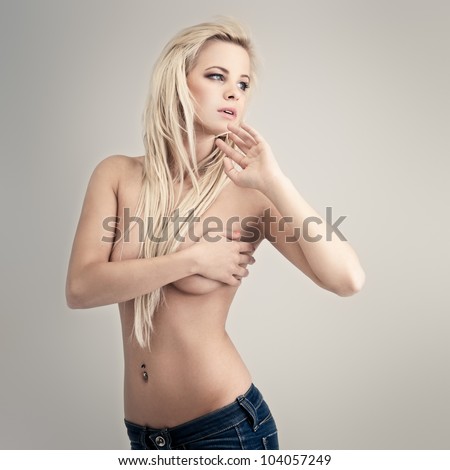 Young topless lady in blue jeans on gray background