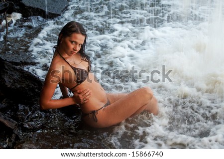 Young lady in bikini laying on stones under waterfalls
