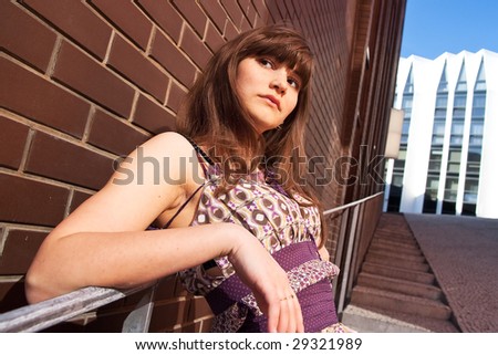 Stylish young woman leans her elbows on hand-rail in a cityscape