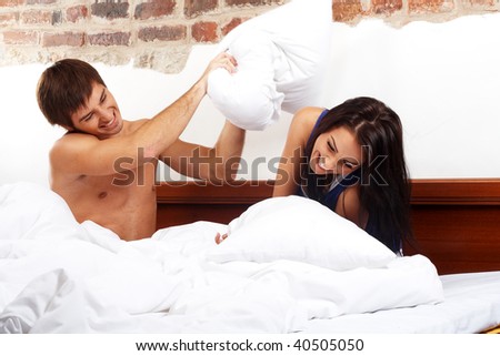 Young happy couple having a pillow fight in a bed