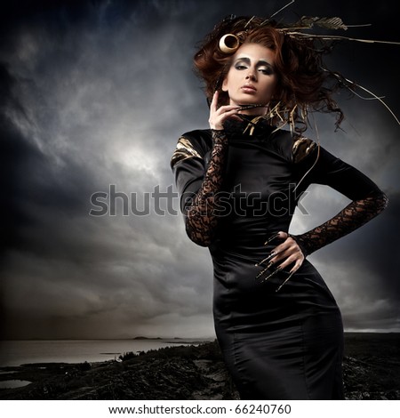 High fashion model in black dress, with long nails and creative hairstyling and makeup in stormy weather
