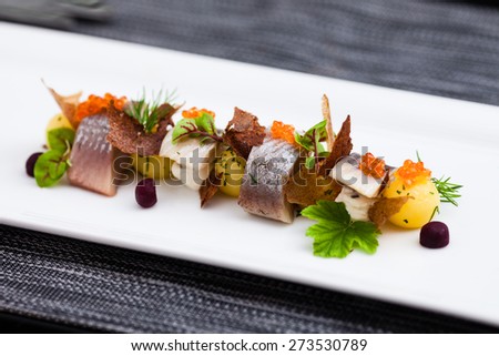 Salted and marinated herring on creamy cheese, beer and black bread chips, potatoes and red caviar