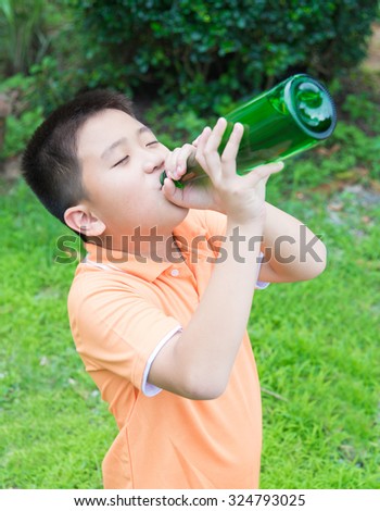 Asian boy drinking water from green bottle, in garden, green background