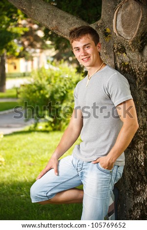 Happy young man standing in summer park at tree