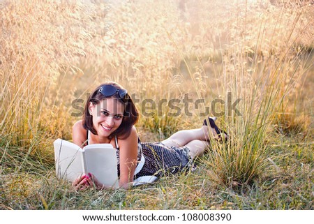 Young attentive woman lies on grass and reads book at summer meadow