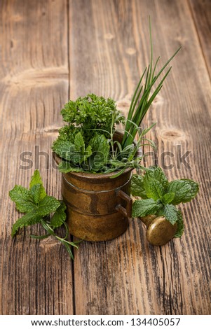 Vintage copper mortar with herbs on rustic wooden background