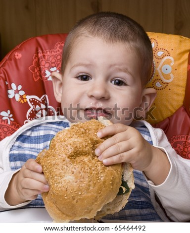 The little happy boy eating a tasty hamburger