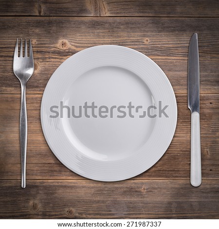 Knife and fork with white plate on a rustic wooden surface