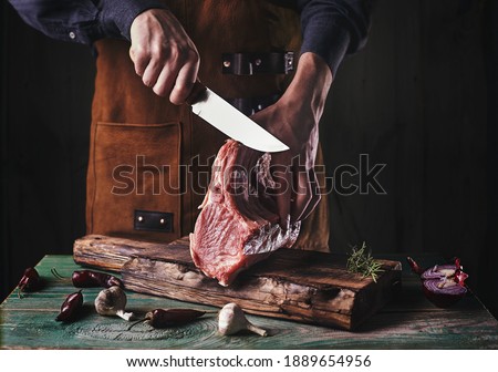 A guy in a leather apron is slicing raw meat. The butcher cuts the pork ribs. Meat with bone on a wooden cutting board. Foto stock © 
