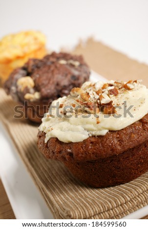 A selection of three muffins on a brown cloth on a white plate in a studio environment