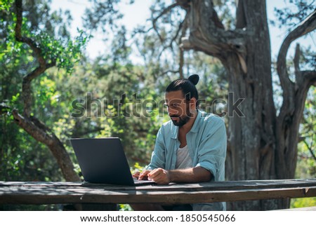 Male tourist working on a laptop outdoors in a camping. Young guy, freelancer working online at a laptop computer on a hike in the mountains outdoors. The ability to work from anywhere in the world. 商業照片 © 